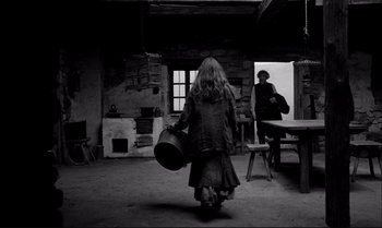 Movie still from “The Turin Horse” (2011), directed by Ágnes Hranitzky – A woman walking in a room with a hat on her head; Wide shot, Over the shoulder angle