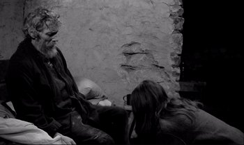 Movie still from “The Turin Horse” (2011), directed by Ágnes Hranitzky – Two people sitting on the ground in front of a stone wall; Medium shot, Over the shoulder angle