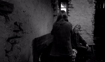 Movie still from “The Turin Horse” (2011), directed by Ágnes Hranitzky – Two people are sitting in a room with a window open; Wide shot, Over the shoulder angle