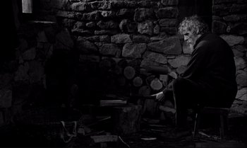 Movie still from “The Turin Horse” (2011), directed by Ágnes Hranitzky – An old man sitting in front of an old fireplace; Medium shot, Over the shoulder angle