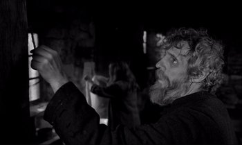 Movie still from “The Turin Horse” (2011), directed by Ágnes Hranitzky – An old man with a long white beard holding something in his hand; Medium shot, Low angle