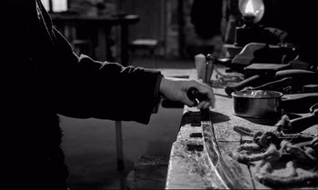 Movie still from “The Turin Horse” (2011), directed by Ágnes Hranitzky – A person holding a pair of scissors on top of a wooden table; Close Up shot, Over the shoulder angle