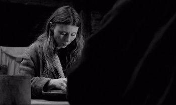 Movie still from “The Turin Horse” (2011), directed by Ágnes Hranitzky – A woman sitting at a table writing on a piece of paper; Medium shot, Over the shoulder angle