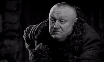 An older man with a shaved head wearing a fur coat