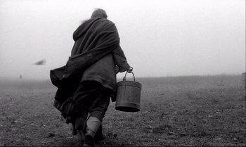 Movie still from “The Turin Horse” (2011), directed by Ágnes Hranitzky – A person walking in a field holding a bucket; Wide shot, Low angle