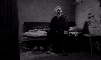 Movie still from “The Turin Horse” (2011), directed by Ágnes Hranitzky – An older man sitting on a bed in a room; Wide shot, High angle