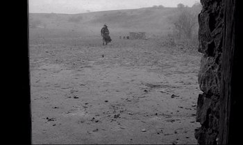 Movie still from “The Turin Horse” (2011), directed by Ágnes Hranitzky – A man walking across a dry grass covered field; Extreme Wide shot, High angle