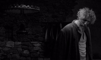 Movie still from “The Turin Horse” (2011), directed by Ágnes Hranitzky – An older man standing in front of a stone wall; Medium shot, Over the shoulder angle