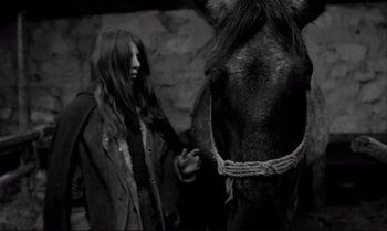 Movie still from “The Turin Horse” (2011), directed by Ágnes Hranitzky – A woman standing next to a horse in a dark room; Medium shot, Low angle