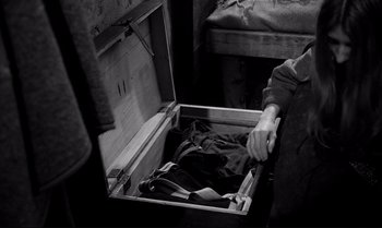 Movie still from “The Turin Horse” (2011), directed by Ágnes Hranitzky – A person opening a suitcase in a room with two beds; Medium shot, High angle