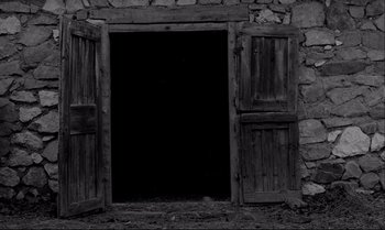 Movie still from “The Turin Horse” (2011), directed by Ágnes Hranitzky – An open door in a stone building with a black background; Wide shot, Low angle