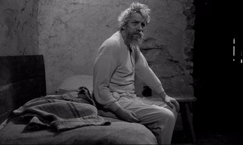 Movie still from “The Turin Horse” (2011), directed by Ágnes Hranitzky – An older man sitting on a bed in a room; Medium shot, High angle