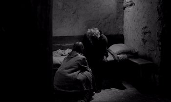 Movie still from “The Turin Horse” (2011), directed by Ágnes Hranitzky – Two people sitting on a bed in a room; Wide shot, High angle