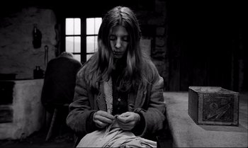 Movie still from “The Turin Horse” (2011), directed by Ágnes Hranitzky – A woman sitting on a bench looking down at a piece of paper; Medium shot, Low angle