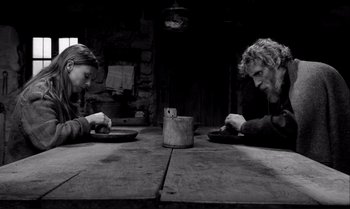 Movie still from “The Turin Horse” (2011), directed by Ágnes Hranitzky – Two people sitting at a wooden table with plates; Medium shot, Over the shoulder angle