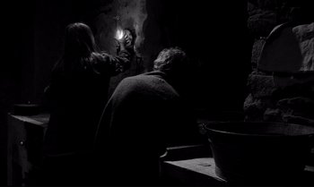 Movie still from “The Turin Horse” (2011), directed by Ágnes Hranitzky – Two people in a dark room with a candle in the dark; Medium shot, Low angle