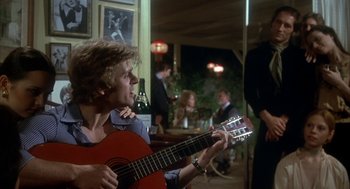 Movie still from “The Turning Point” (1977), directed by Herbert Ross – A man holding a guitar while standing in a room; Medium shot, Over the shoulder angle