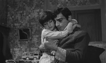 Movie still from “The Two of Us” (1967), directed by Claude Berri – A man and a boy are hugging in a living room; Medium shot, High angle