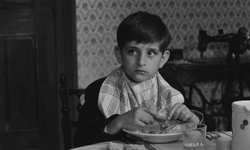 Movie still from “The Two of Us” (1967), directed by Claude Berri – A boy sitting at a table eating a plate of food; Close Up shot, Over the shoulder angle