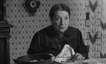 Movie still from “The Two of Us” (1967), directed by Claude Berri – An older woman sitting at a table with a plate in front of her; Close Up shot, Over the shoulder angle