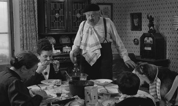 Movie still from “The Two of Us” (1967), directed by Claude Berri – An old man standing at a table with a bunch of people; Medium shot, High angle