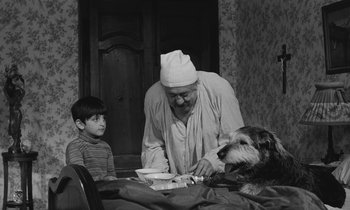 Movie still from “The Two of Us” (1967), directed by Claude Berri – An old man and a boy and a dog are sitting at a table; Medium shot, Over the shoulder angle