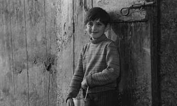 Movie still from “The Two of Us” (1967), directed by Claude Berri – A young boy holding a bowl in front of a wooden wall; Medium shot, High angle