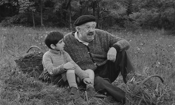 Movie still from “The Two of Us” (1967), directed by Claude Berri – An older man and a young boy sitting on the grass; Medium shot, Low angle