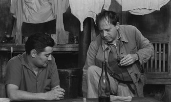 Movie still from “The Two of Us” (1967), directed by Claude Berri – Two men sitting at a table with a bottle of wine; Medium shot, Low angle