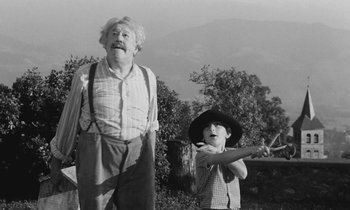 Movie still from “The Two of Us” (1967), directed by Claude Berri – An older man and a young boy are standing in a field; Medium shot, Low angle