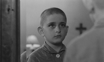 Movie still from “The Two of Us” (1967), directed by Claude Berri – A young boy with a shaved head looks at the camera; Close Up shot, Over the shoulder angle