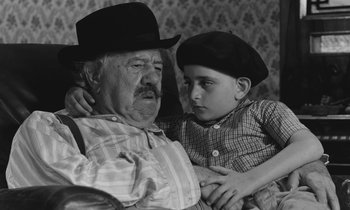 Movie still from “The Two of Us” (1967), directed by Claude Berri – An older man and a young boy sitting next to each other; Medium shot, High angle