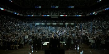 Movie still from “House of Cards” (2013), created by Beau Willimon – A crowd of people are gathered in a stadium to watch a political event; Extreme Wide shot, High angle