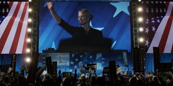 Movie still from “House of Cards” (2013), created by Beau Willimon – A woman is raising her hand in front of a large screen; Wide shot, Low angle