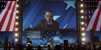 Movie still from “House of Cards” (2013), created by Beau Willimon – An older woman standing in front of an american flag; Wide shot, Low angle
