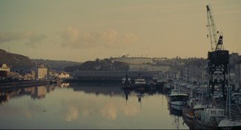 Movie still from “The Umbrellas of Cherbourg” (1964), directed by Jacques Demy – Several boats are docked in the water near the shore; Extreme Wide shot, High angle