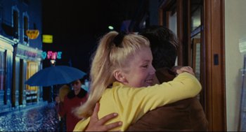 Movie still from “The Umbrellas of Cherbourg” (1964), directed by Jacques Demy – A woman is hugging a man in a yellow shirt; Medium shot, Over the shoulder angle