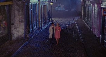 Movie still from “The Umbrellas of Cherbourg” (1964), directed by Jacques Demy – A man and a woman walking down a street at night; Wide shot, High angle
