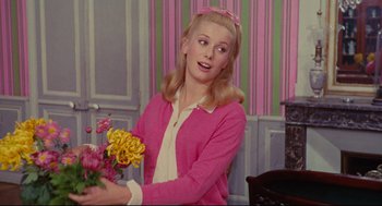 Movie still from “The Umbrellas of Cherbourg” (1964), directed by Jacques Demy – A woman in a pink sweater holding a bouquet of flowers; Medium shot, Over the shoulder angle