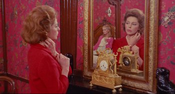 Movie still from “The Umbrellas of Cherbourg” (1964), directed by Jacques Demy – A woman looking in the mirror in front of a clock; Medium shot, High angle