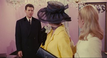 Movie still from “The Umbrellas of Cherbourg” (1964), directed by Jacques Demy – A woman wearing a black hat and a yellow coat; Medium shot, Over the shoulder angle