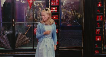 Movie still from “The Umbrellas of Cherbourg” (1964), directed by Jacques Demy – A young girl standing in front of a store window; Medium shot, Over the shoulder angle