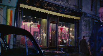 Movie still from “The Umbrellas of Cherbourg” (1964), directed by Jacques Demy – A car parked in front of a store window; Wide shot, High angle