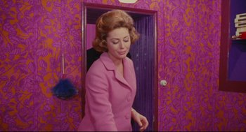 Movie still from “The Umbrellas of Cherbourg” (1964), directed by Jacques Demy – A woman in a pink coat standing in front of a door; Medium shot, High angle