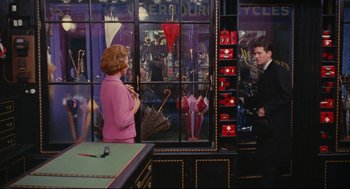 Movie still from “The Umbrellas of Cherbourg” (1964), directed by Jacques Demy – A man and a woman are looking at each other through a store window; Wide shot, High angle