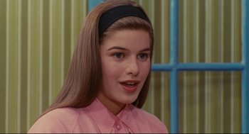 Movie still from “The Umbrellas of Cherbourg” (1964), directed by Jacques Demy – A young woman with a headband is smiling for the camera; Close Up shot, Over the shoulder angle