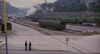 Movie still from “The Umbrellas of Cherbourg” (1964), directed by Jacques Demy – Two men standing on a train track next to train tracks; Extreme Wide shot, High angle