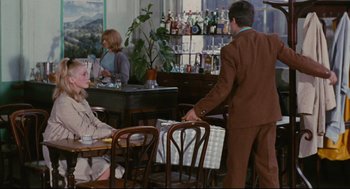 Movie still from “The Umbrellas of Cherbourg” (1964), directed by Jacques Demy – A man in a brown suit is standing at a bar; Wide shot, Over the shoulder angle