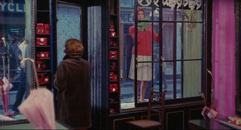 Movie still from “The Umbrellas of Cherbourg” (1964), directed by Jacques Demy – A woman standing in front of a store looking out the window; Wide shot, Over the shoulder angle