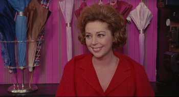 Movie still from “The Umbrellas of Cherbourg” (1964), directed by Jacques Demy – A woman in a red jacket smiling for the camera; Close Up shot, Over the shoulder angle